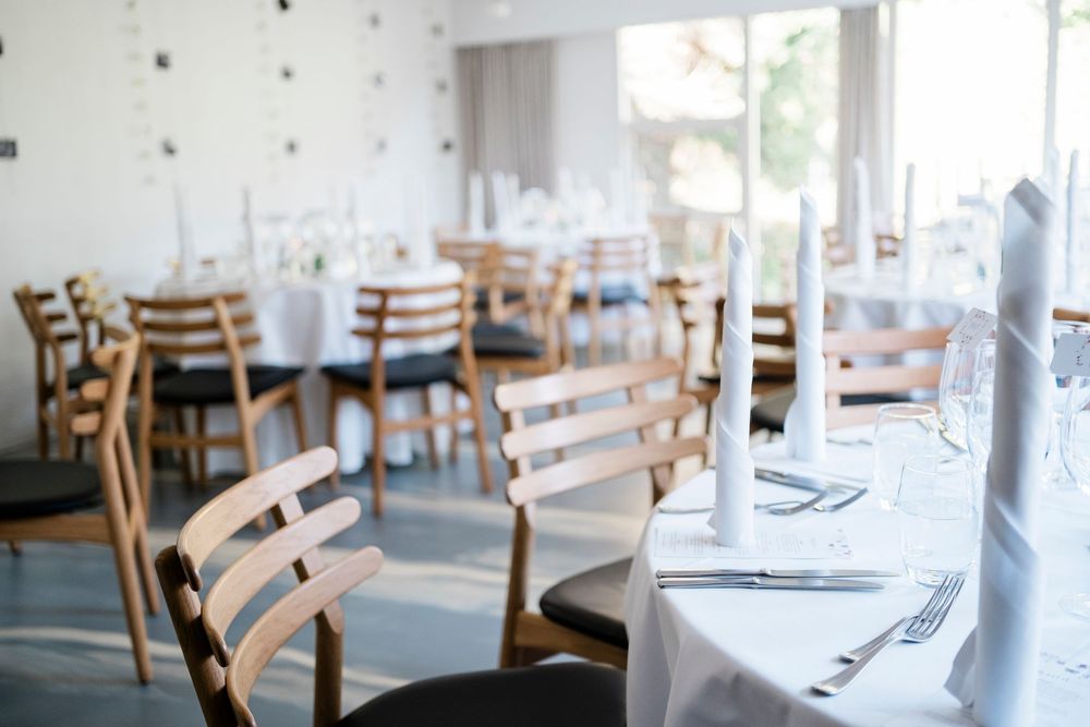 Elegant restaurant dining room with wooden chairs, white tablecloths, candles, and glassware set for a formal occasion.