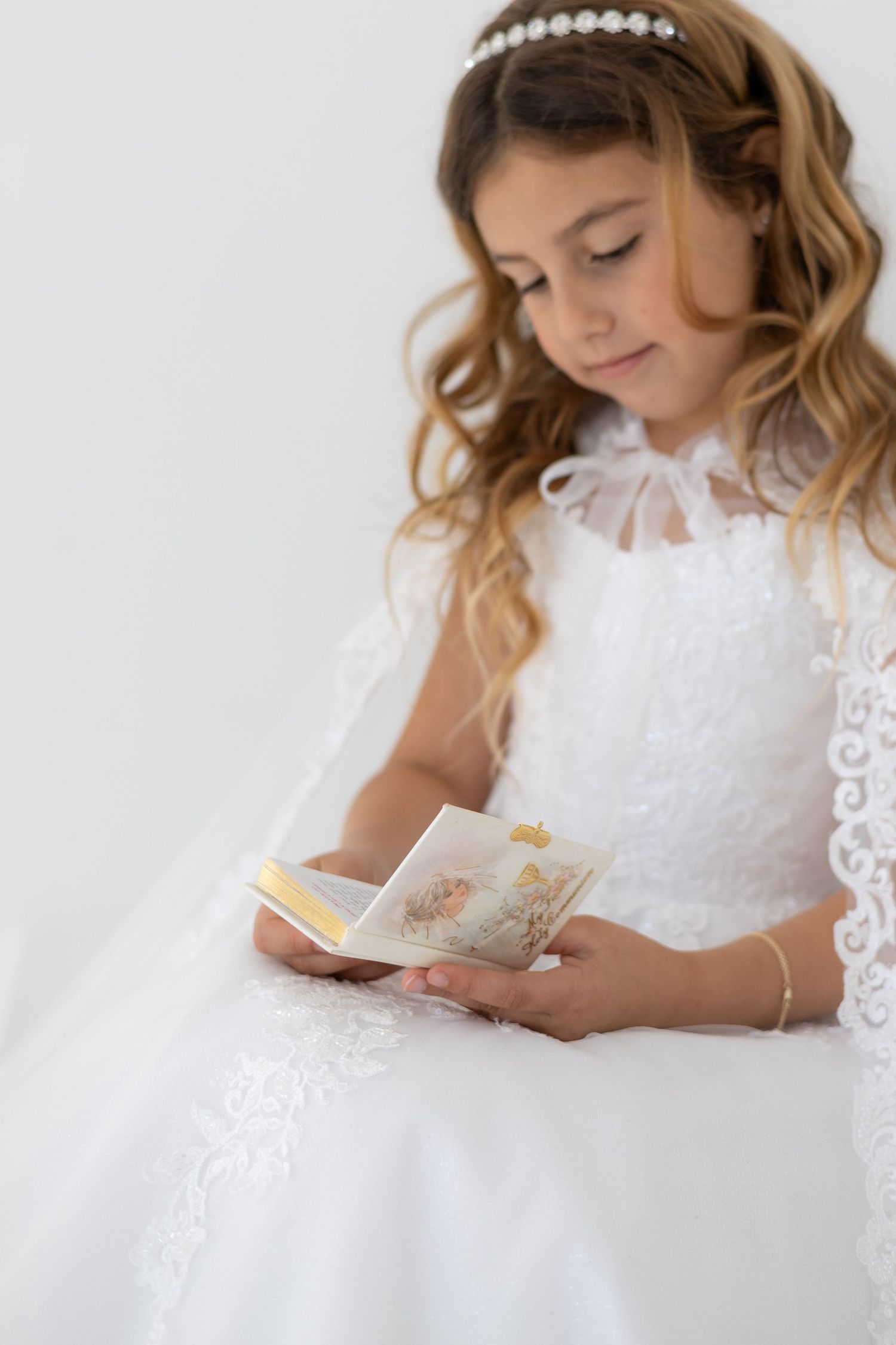 Child in white suit holding rosary beads in prayer position for First Communion ceremony.