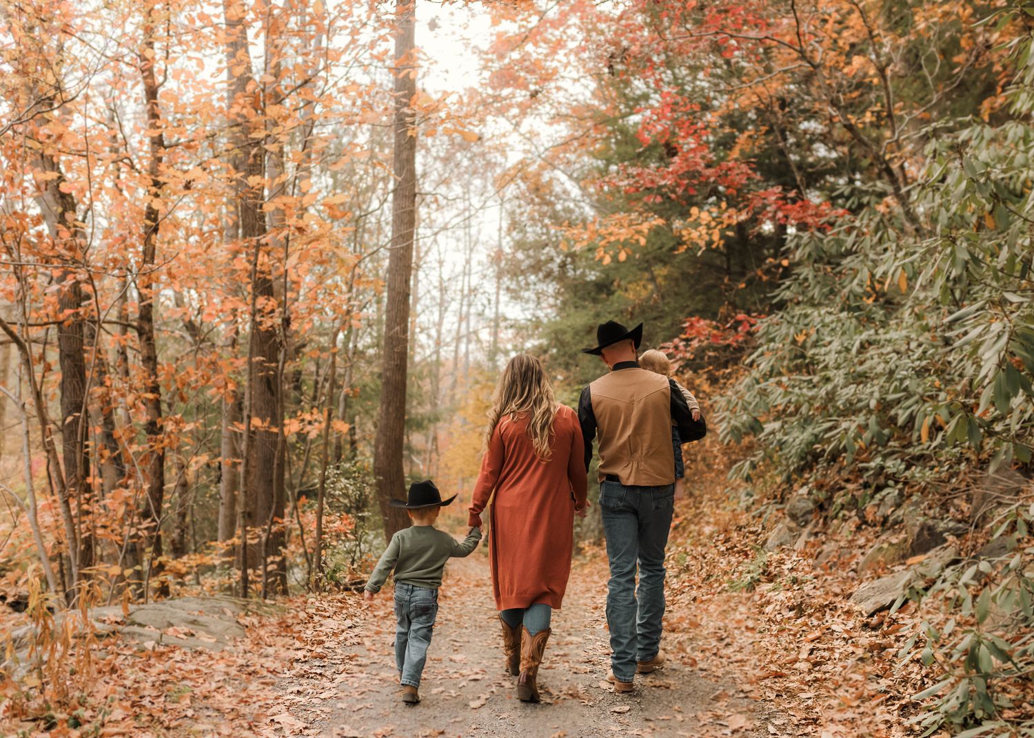 Family walking hand-in-hand on an autumn forest path surrounded by vibrant orange and red foliage.