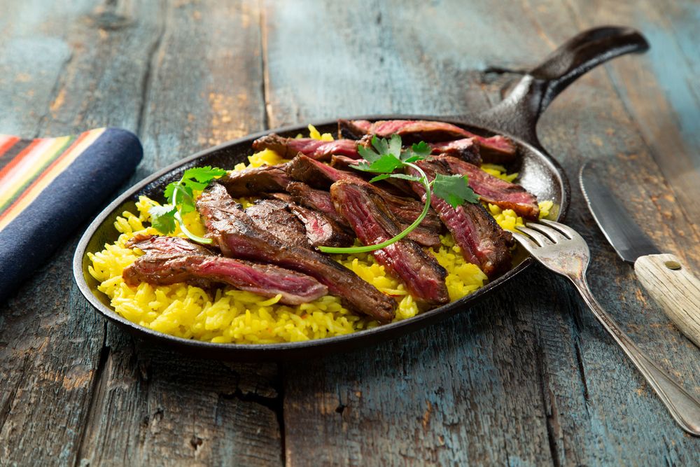 Sliced grilled skirt steak served over saffron yellow rice in a cast iron skillet.