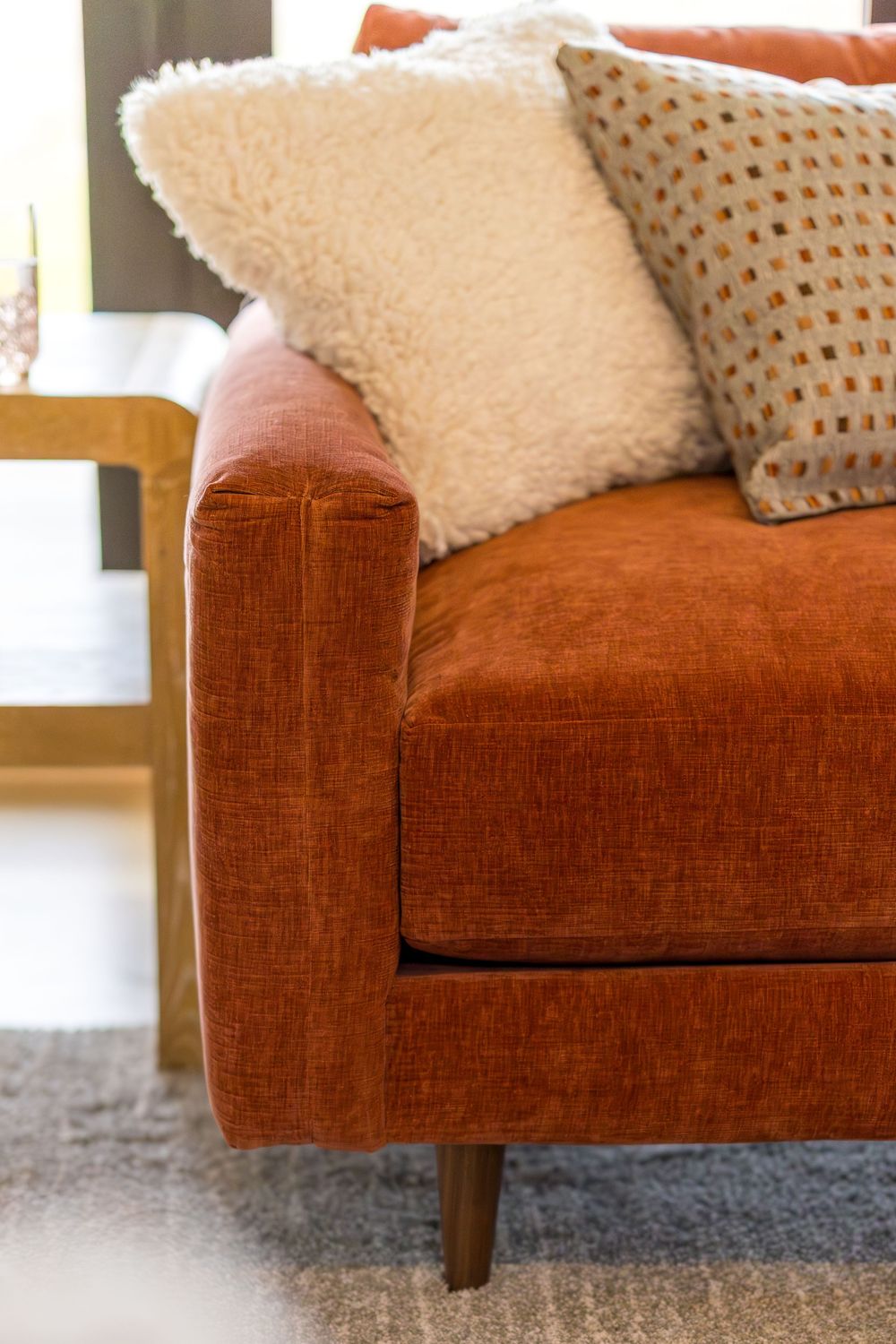 Close-up of rust orange velvet sofa with decorative throw pillows in a modern living room setting.