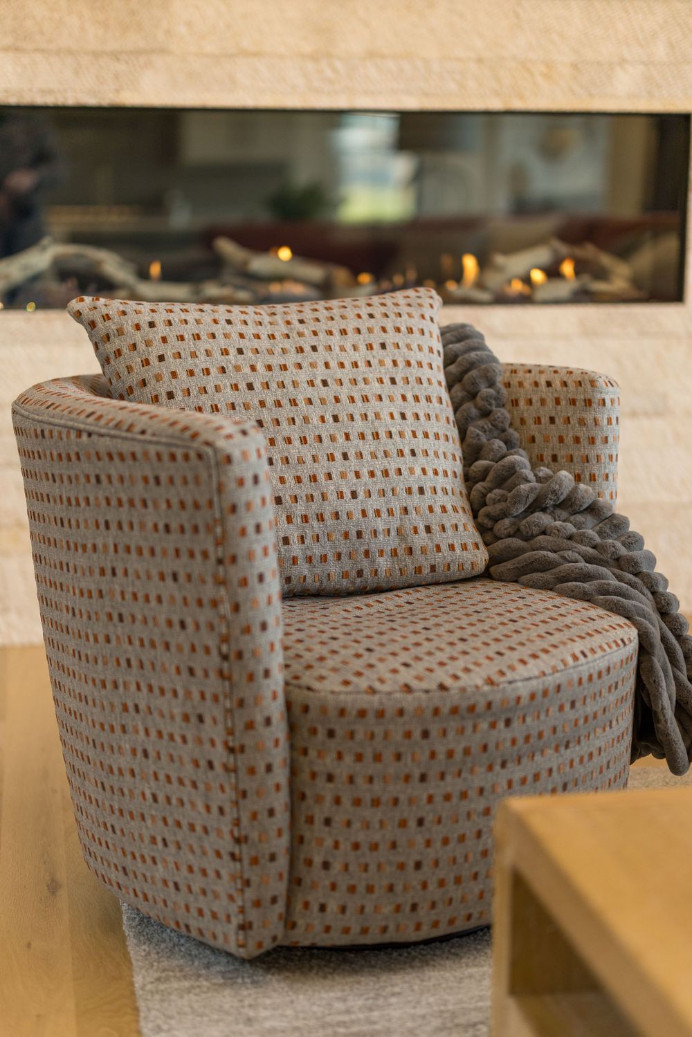Patterned swivel accent chair with matching pillow and knit throw near modern fireplace.