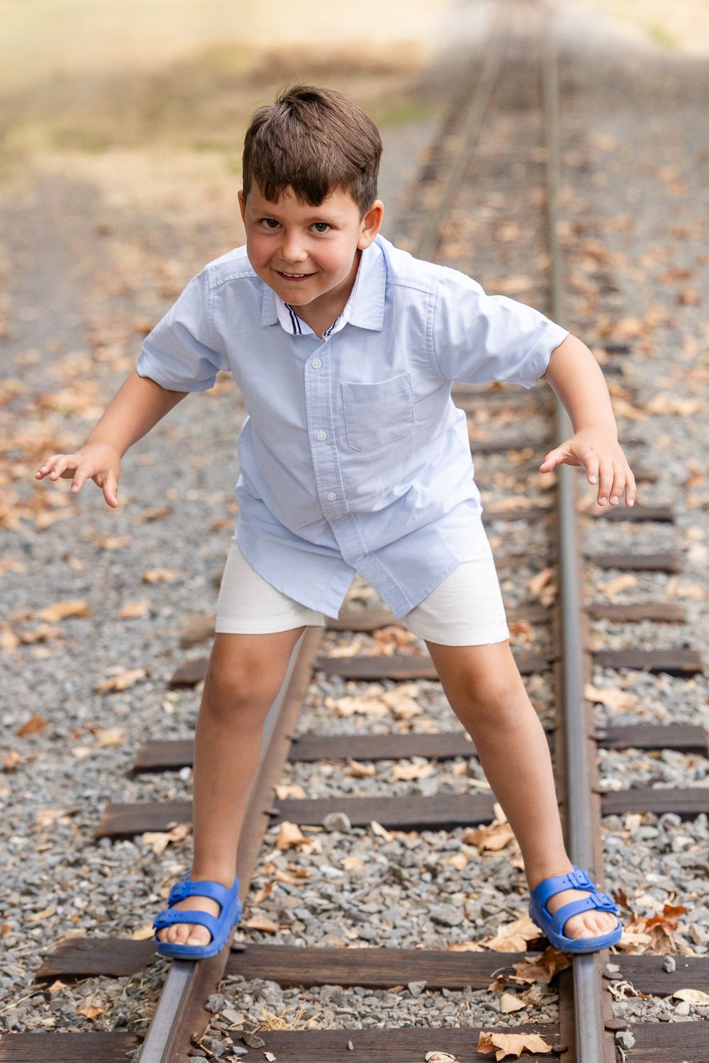 A boy smiles while balancing on train tracks at his family session in Los Gatos