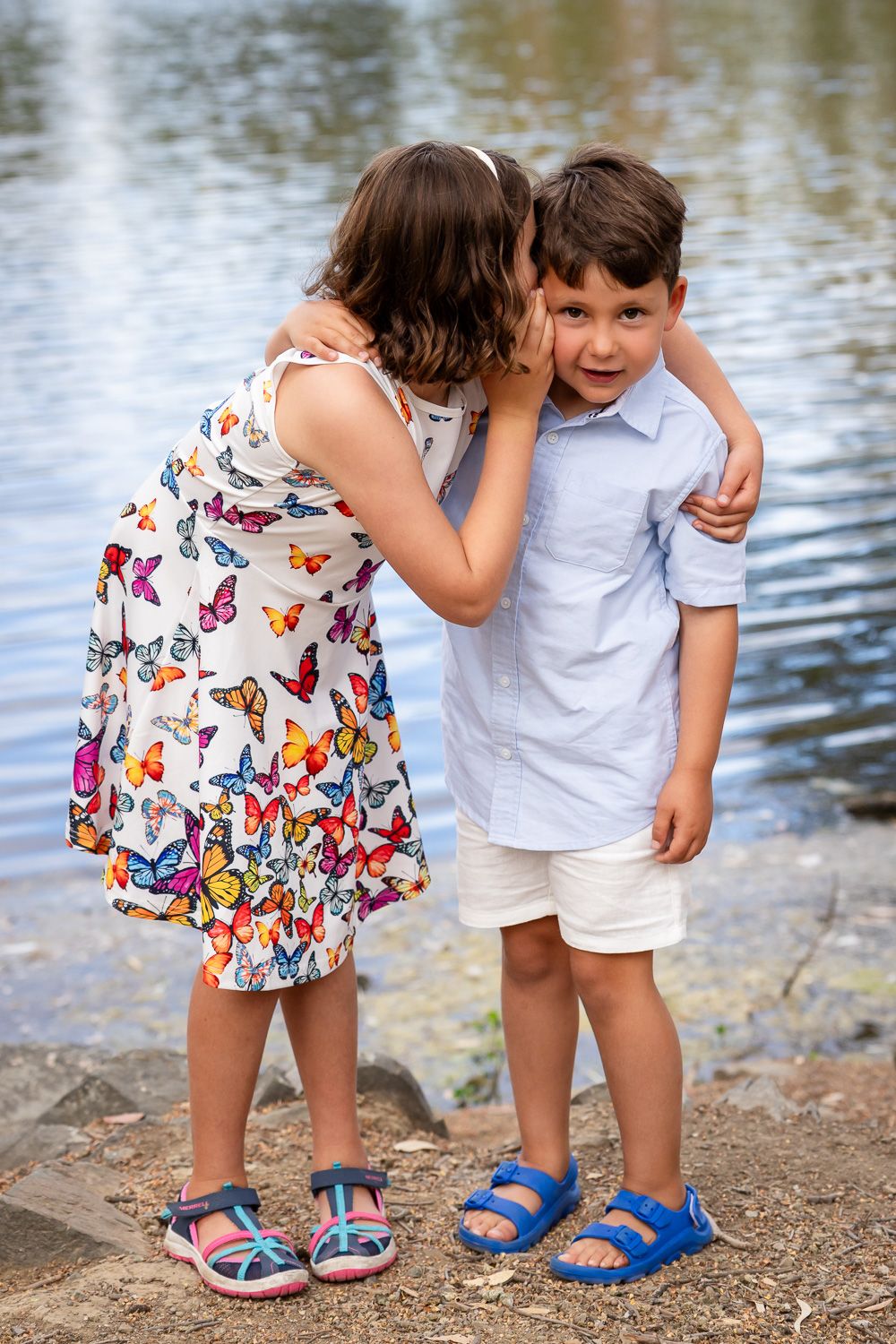 A girl tells her brother a secret in front of the lake