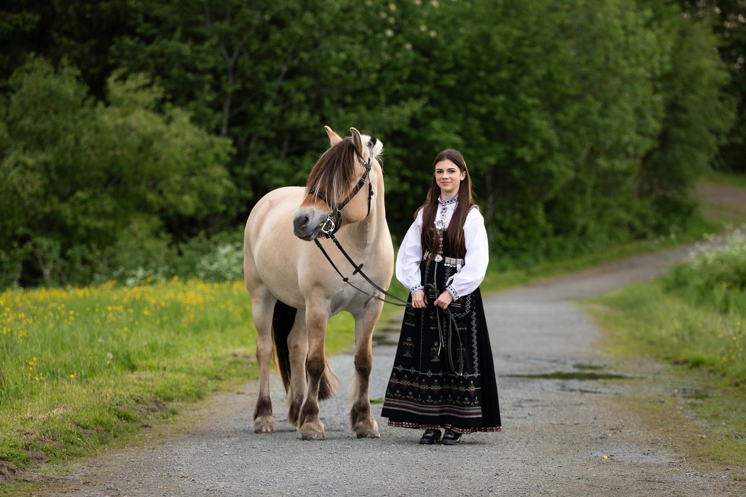 Young woman in traditional folk costume smiling with a palomino horse in a sunny meadow.