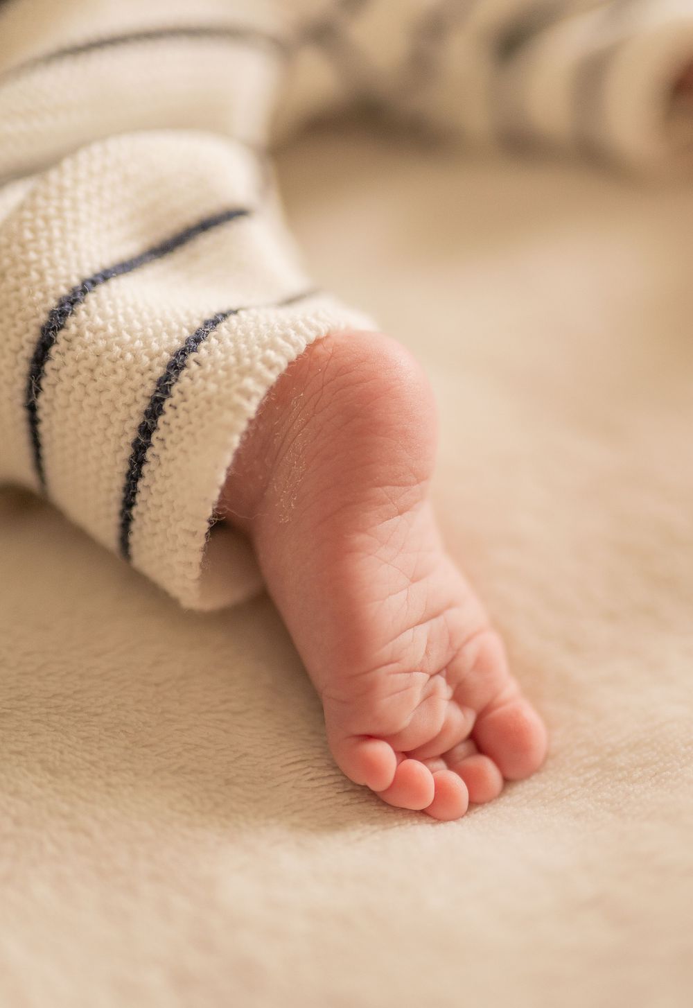Gros plan d'un petit pied de bébé nouveau-né en combinaison rayée sur une couverture beige douce à Rennes en Bretagne.