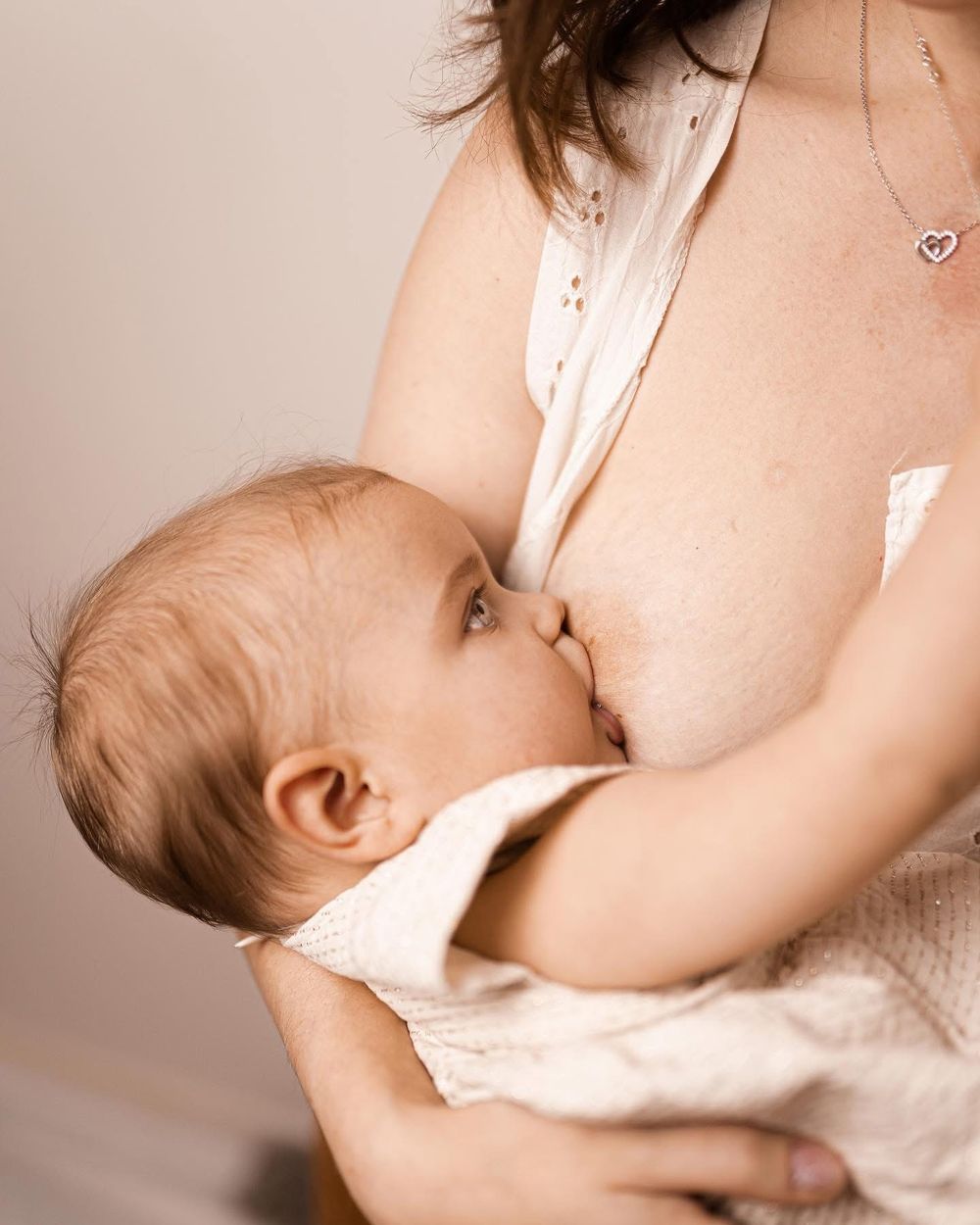 Mère allaitant bébé tout en portant une robe blanche et un collier en forme de cœur à Pontorson.