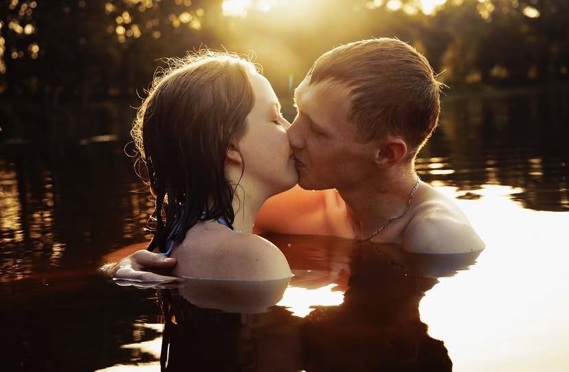Couple romantique s'embrassant dans l'eau dorée du lac ensoleillé au coucher du soleil en Normandie.