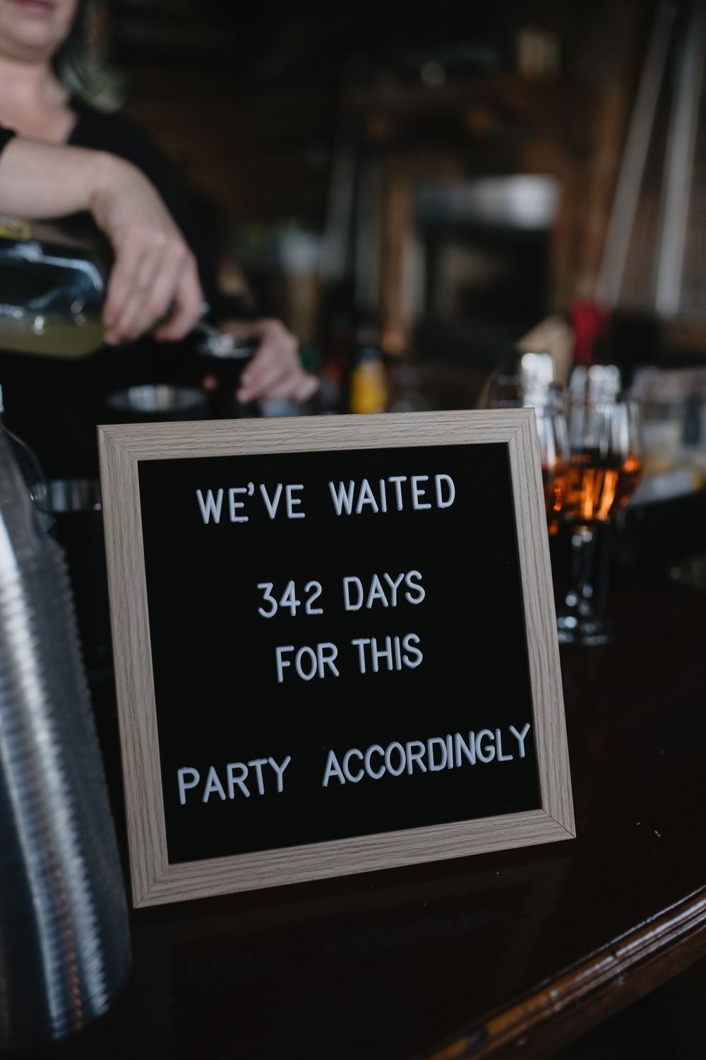 A bar sign reads 'We've waited 342 days for this, party accordingly' with a bartender pouring drinks in the background.