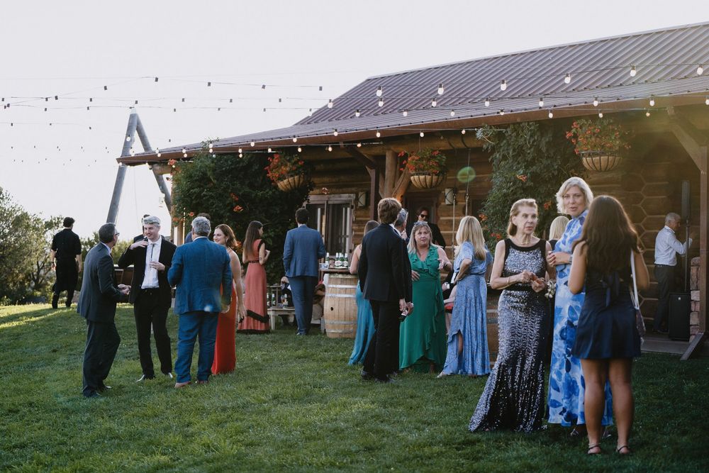 Guests mingling outdoors at rustic barn wedding reception with string lights at dusk.