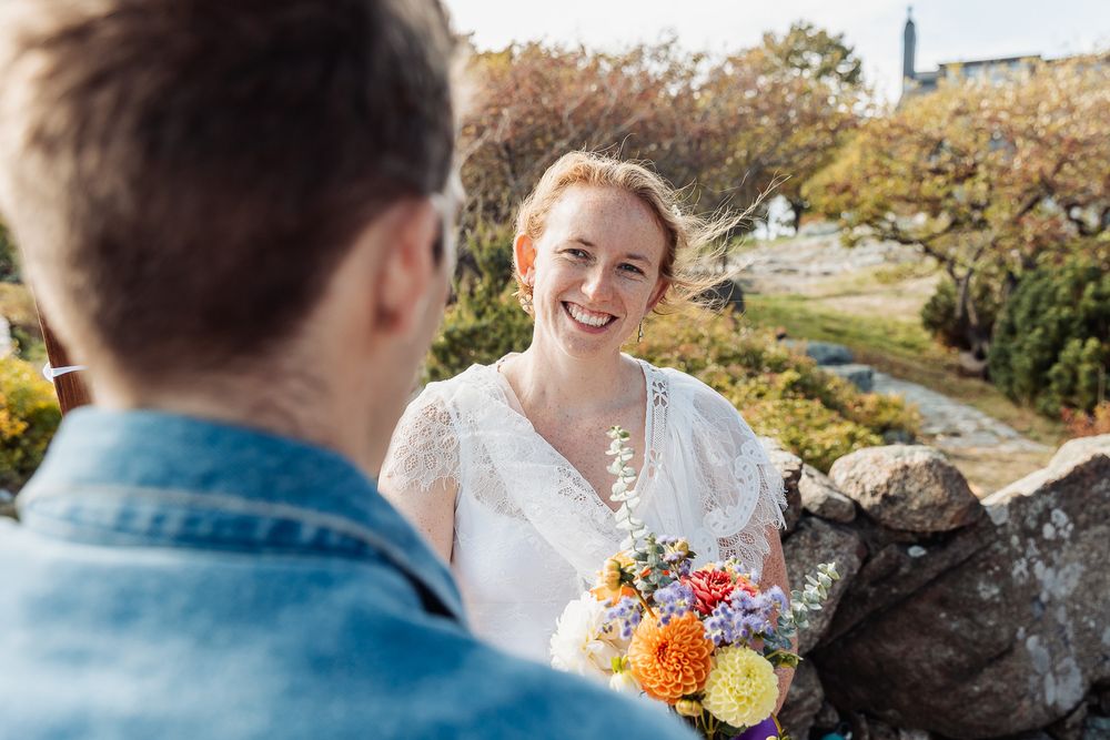 Smiling bride in white dress holding colorful bouquet outdoors on sunny day.