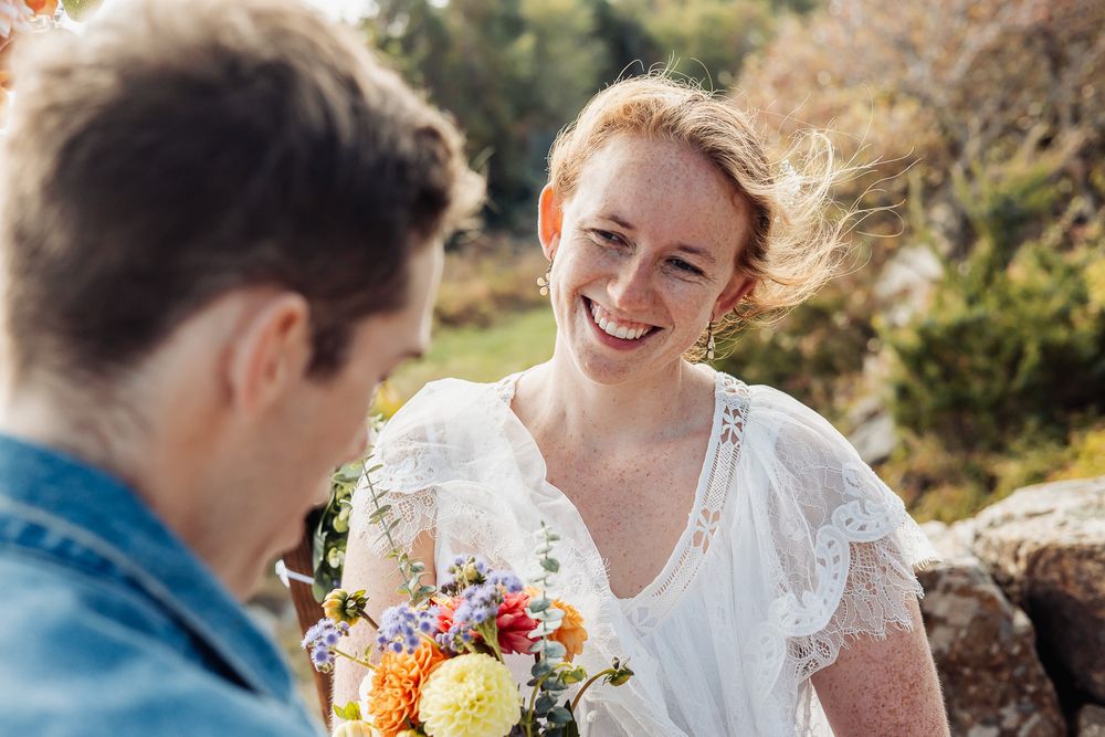 Smiling red-haired bride in white dress holding colorful bouquet with dahlias outdoors on her wedding day.