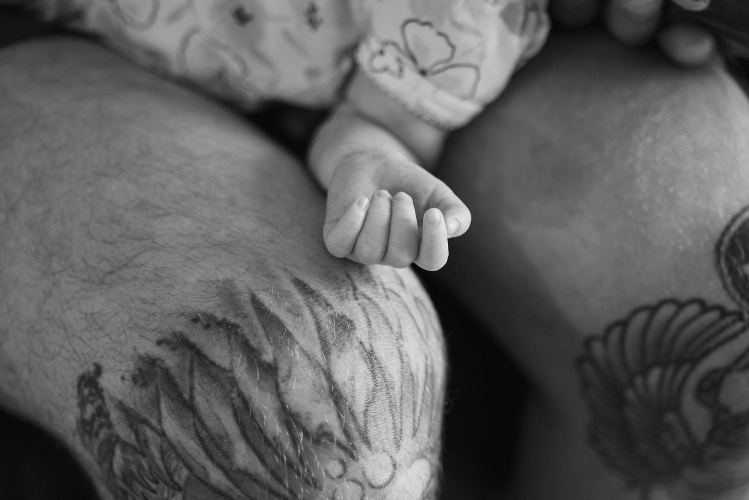 Black and white photo of a newborn baby's tiny hand resting on a parent's leg.