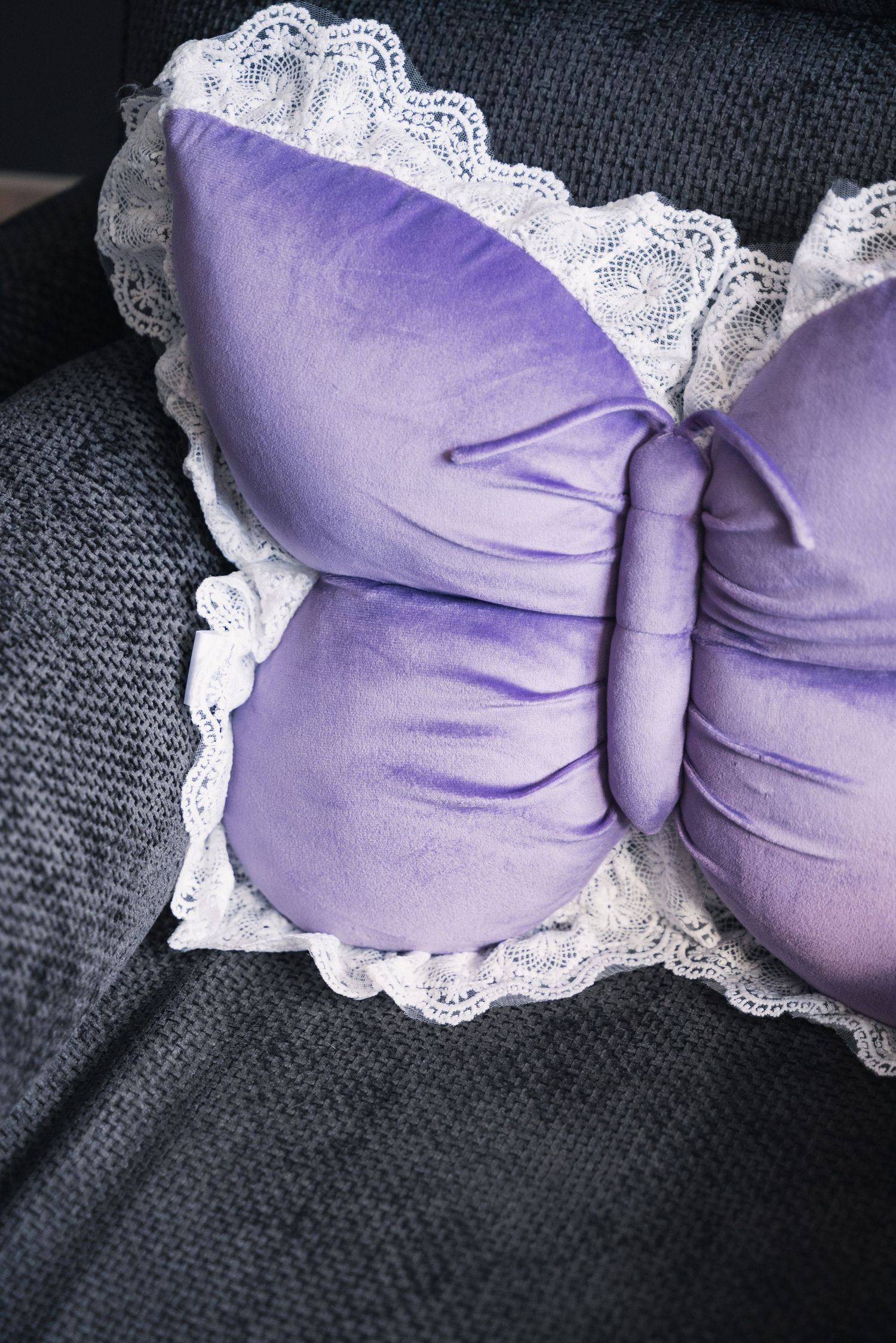 Purple velvet butterfly-shaped pillow with white lace trim on a gray textured surface.