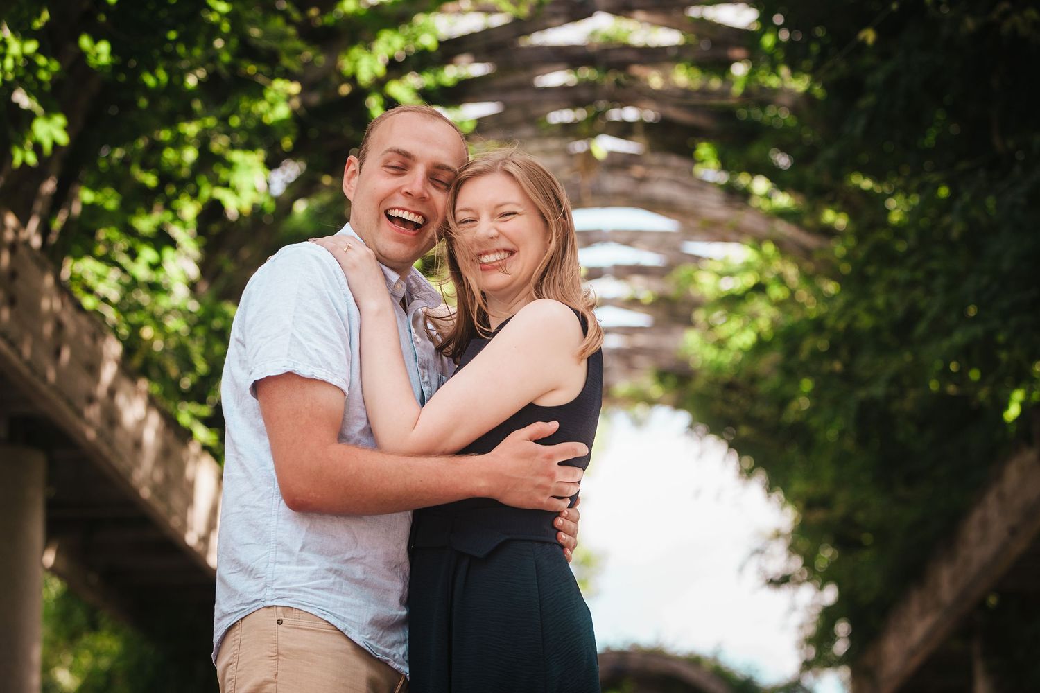Engaged couple laughing together under the trellis at Christopher Columbus Park in Boston's North End