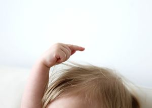 Close-up of a toddler pointing finger upward with fine blonde hair against white background.