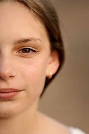 Close-up half portrait of a young girl with brown eyes, freckles, and a gold stud earring.