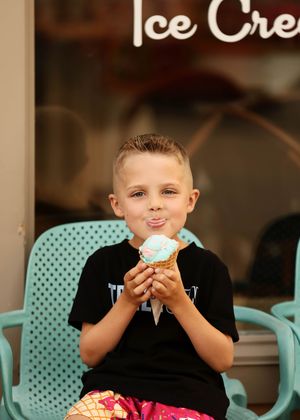 Young boy smiling and enjoying a blue ice cream cone in a waffle cone outside an ice cream shop.