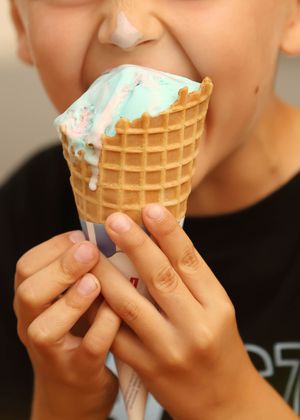 Child licking a blue ice cream waffle cone with dripping melted ice cream.