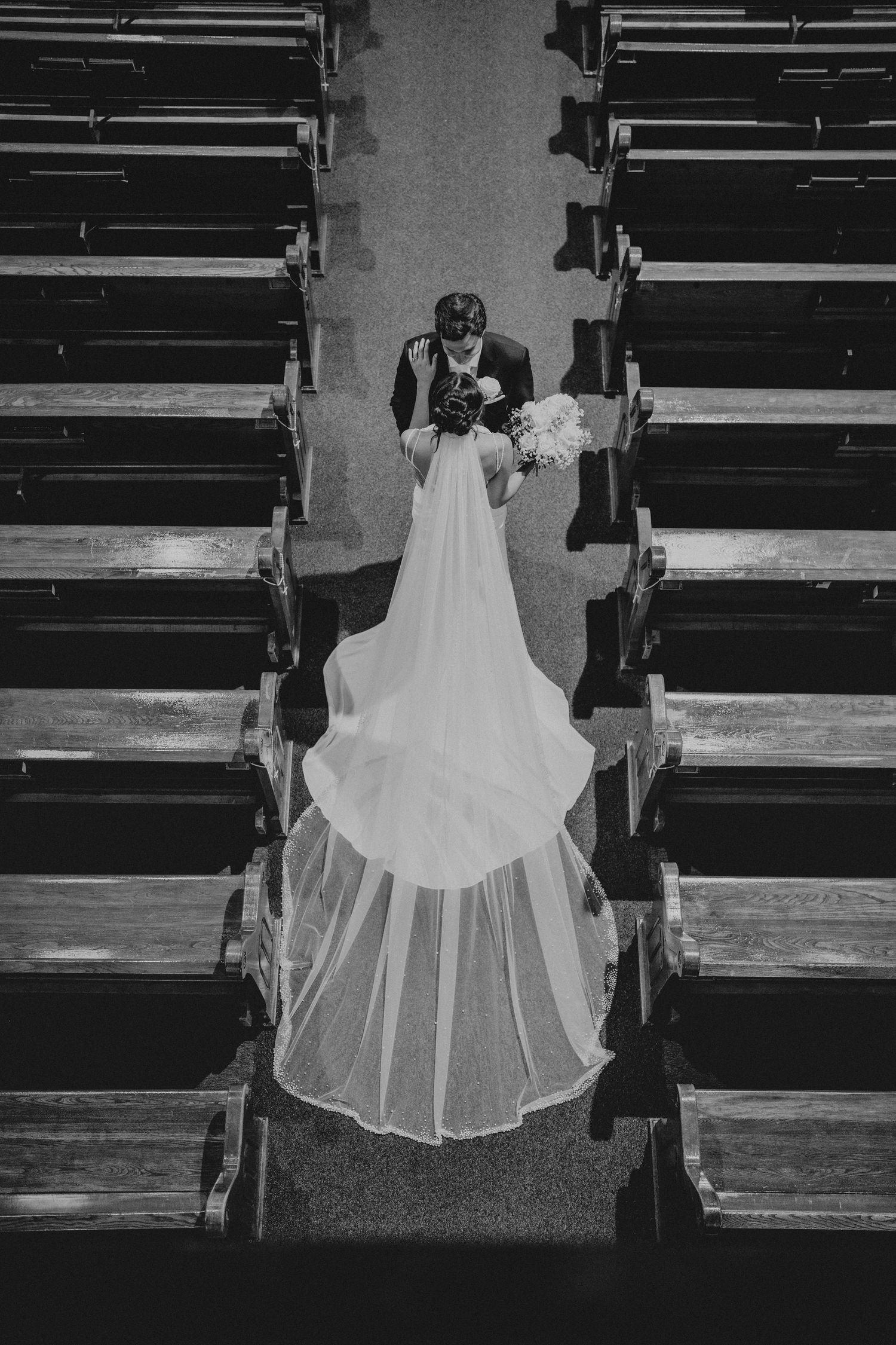 Aerial black and white photo of bride and groom walking down church aisle, bridal veil trailing elegantly behind.