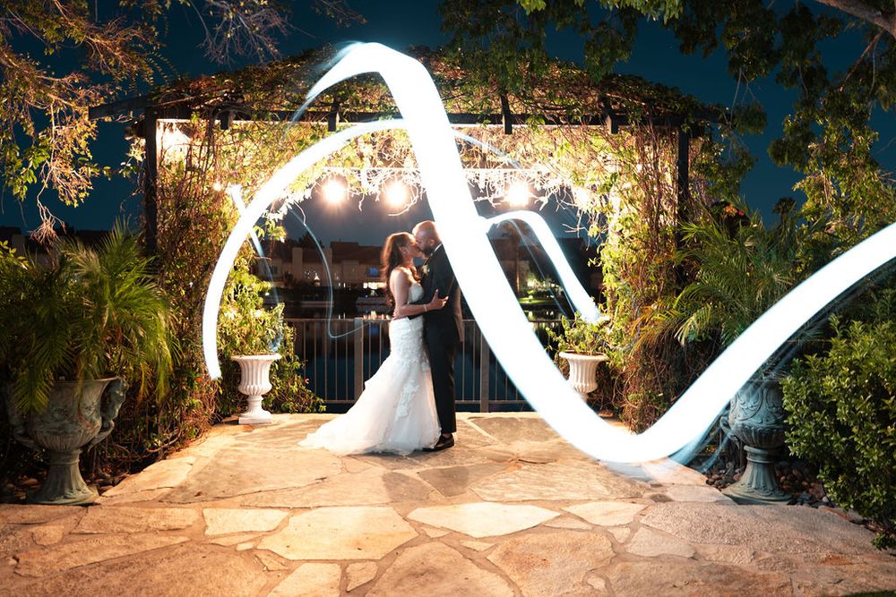 Bride and groom share romantic moment under glowing garden arch with light painting swirl at night wedding.