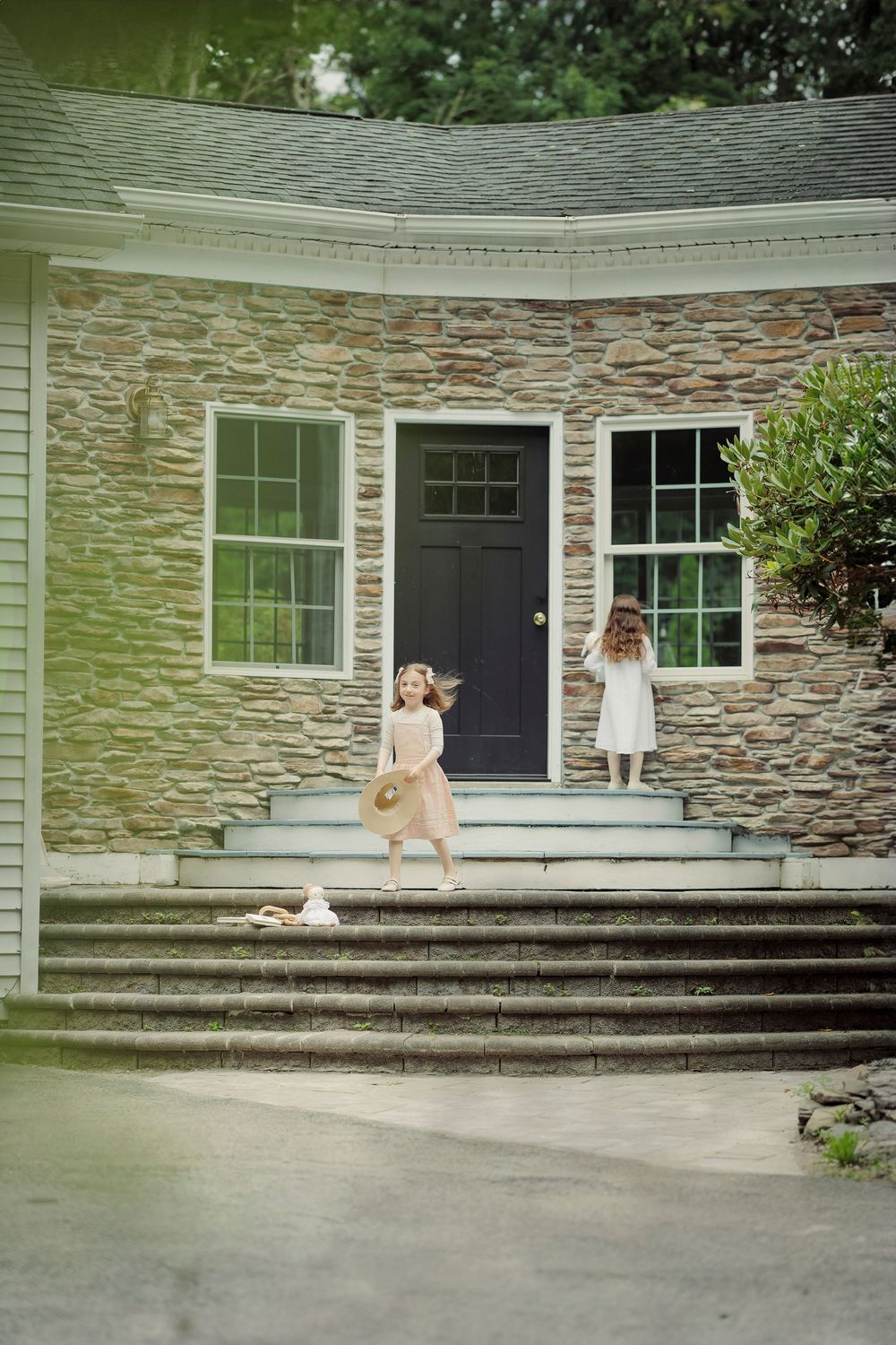 Two girls in dresses playing on stone steps outside a charming curved stone house with a black front door.