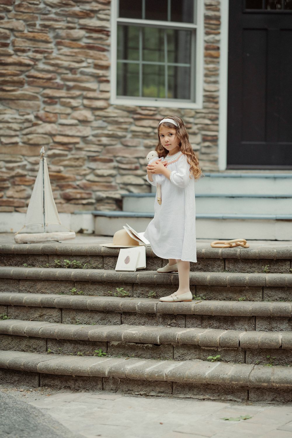 Young girl in white dress holding toy on stone steps.