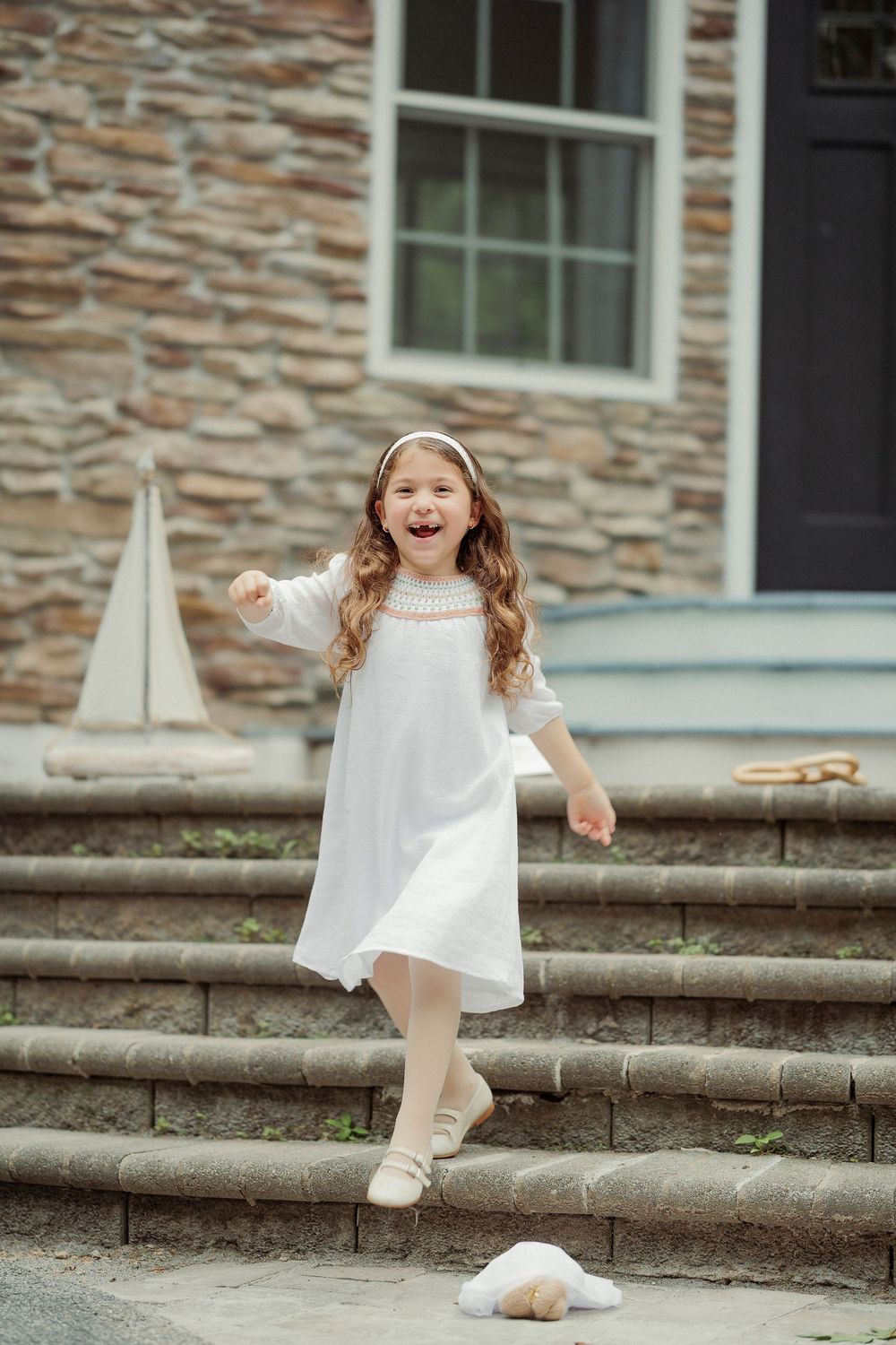 Happy girl in white dress laughing on stone steps outdoors.