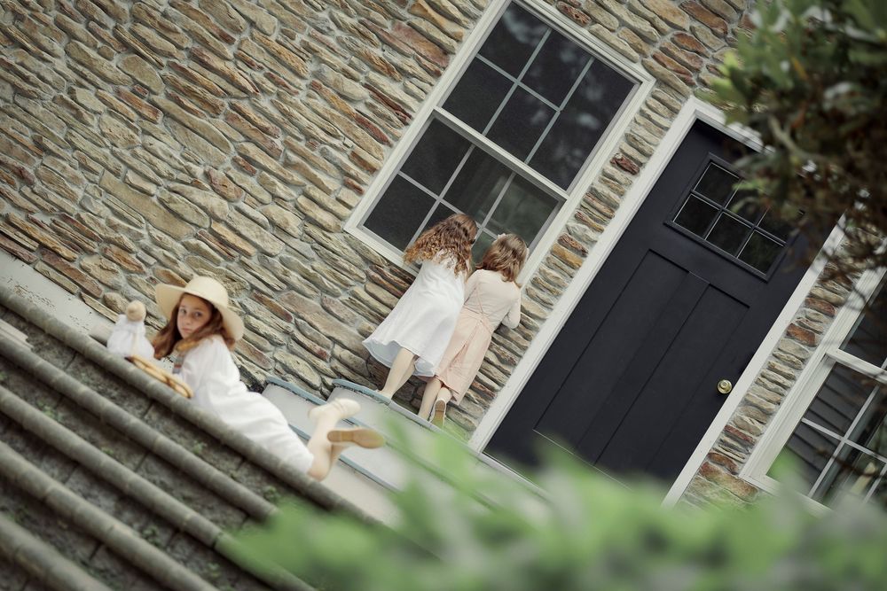 Three women in white outfits relaxing on stone steps outside a rustic building with a black door.