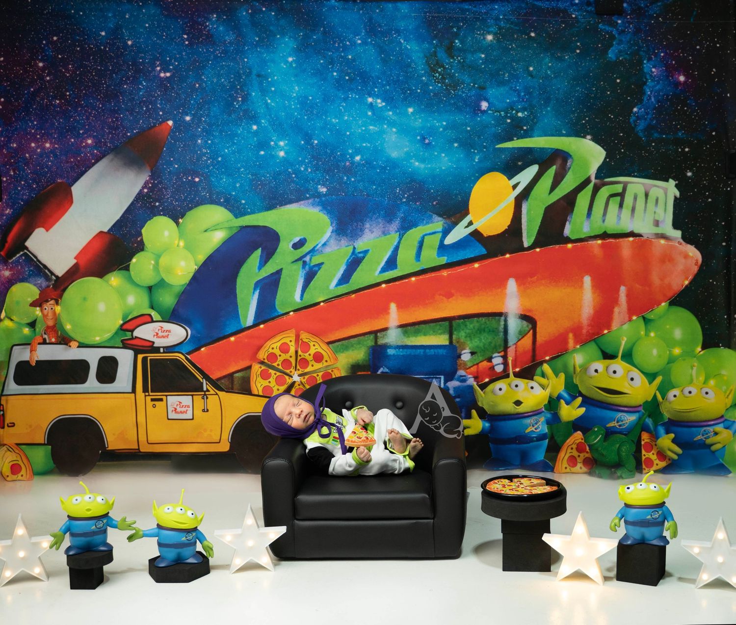 Toy Story Pizza Planet themed birthday setup with alien figurines, a sleeping baby, and colorful galaxy backdrop.