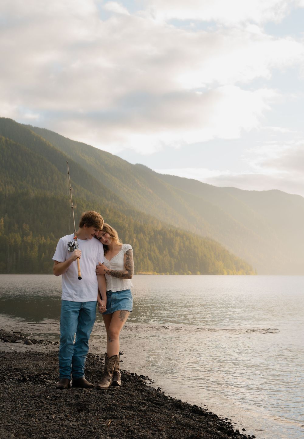 A romantic couple shares a tender moment while fishing on a serene mountain lake at golden hour.