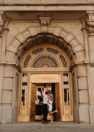 Couple sharing a romantic kiss in golden ornate doorway of elegant historic building.