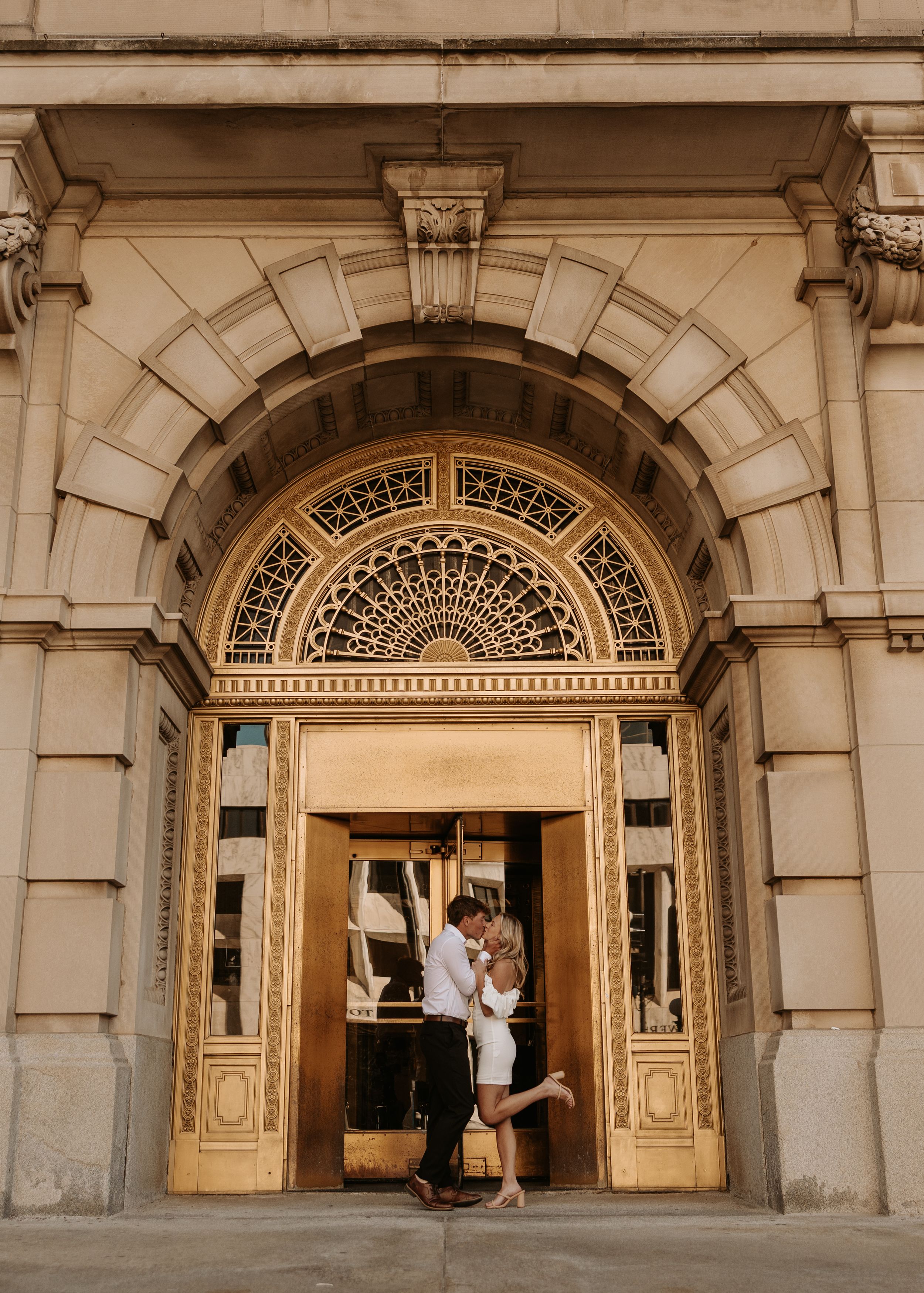 Couple sharing a romantic kiss in golden ornate doorway of elegant historic building.