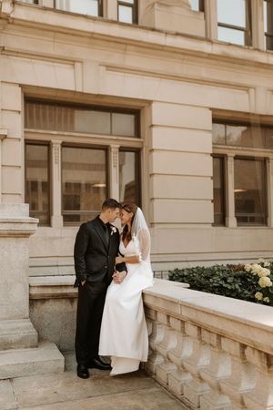 Bride and groom share a romantic moment on stone steps outside a classic building, bride in white gown with veil.