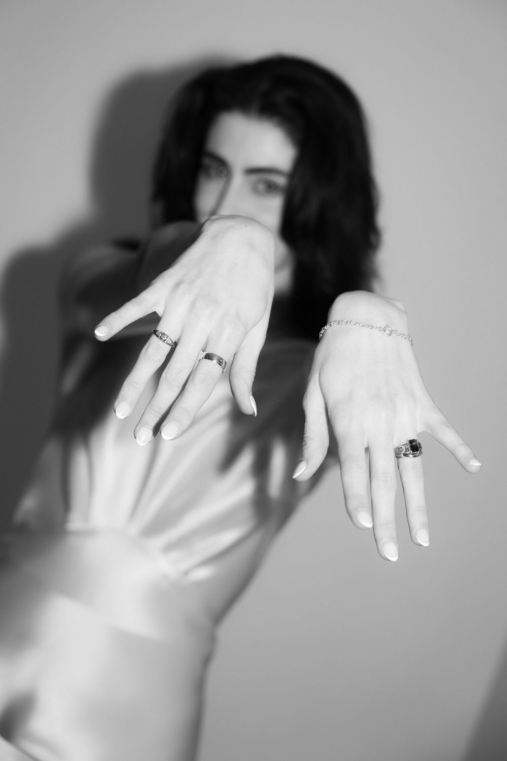 Black and white photo of a woman extending both hands toward camera, wearing rings and a bracelet.