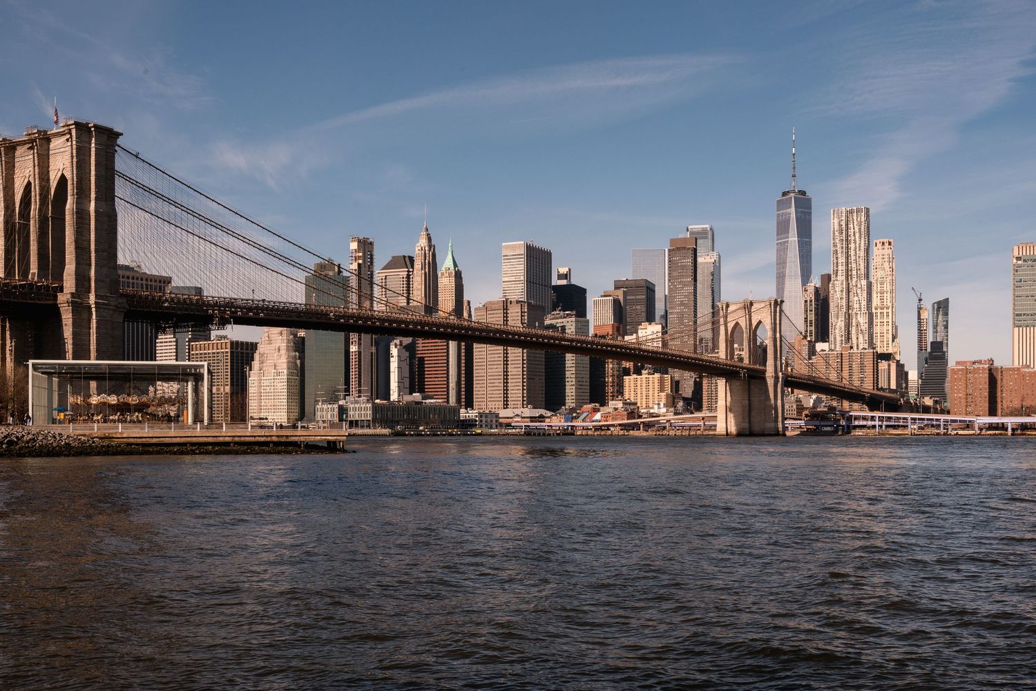 Vista panoramica diurna del ponte di Brooklyn e dei grattacieli finanziari di New York sotto un cielo azzurro.