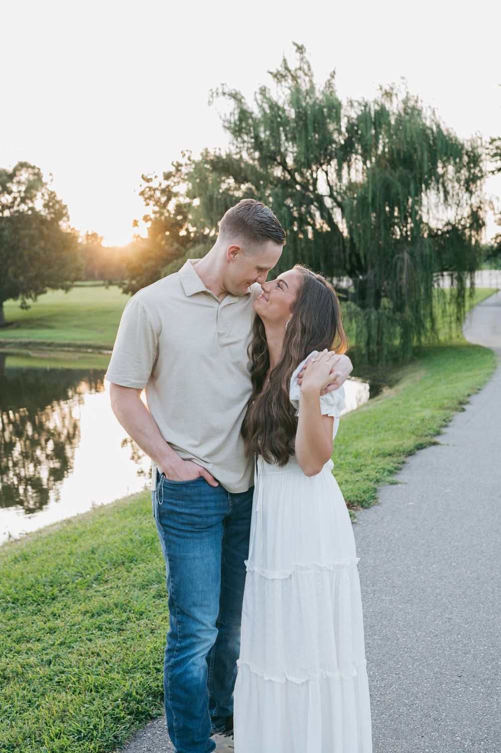 Couple sharing a romantic moment near a reflective pond under a weeping willow at sunset, engagement photographer Mooresville NC