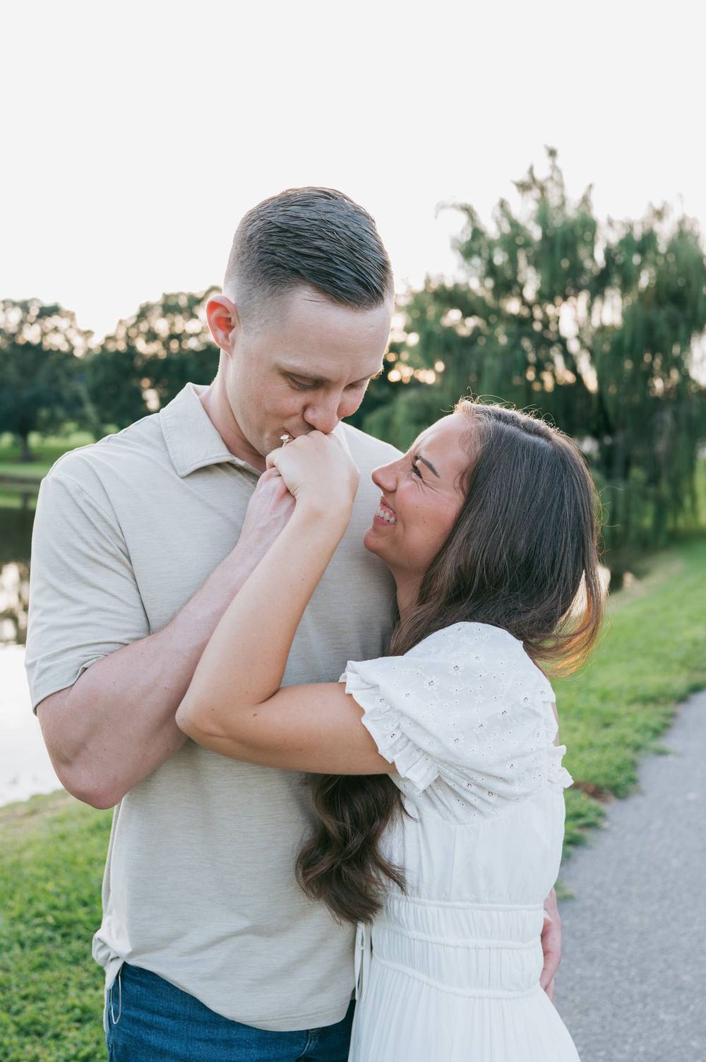 Man kisses woman's hand as she laughs joyfully during an outdoor engagement photo session, engagement photographer Mooresville NC