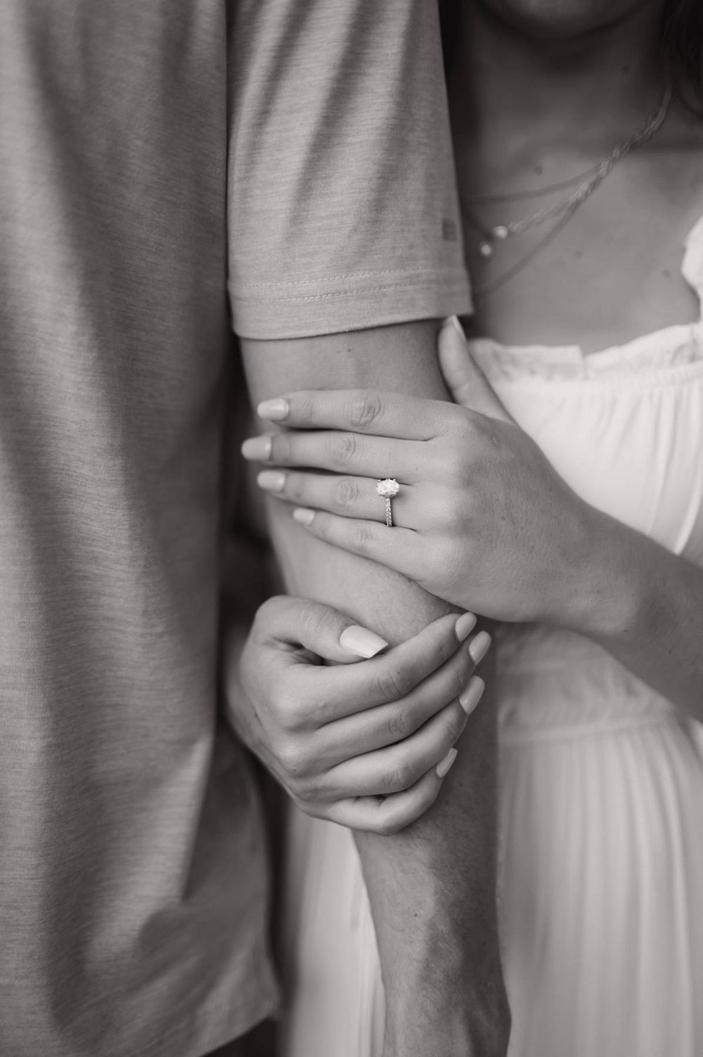 Close-up black and white photo of engaged couple holding hands, diamond engagement ring visible on womans finger, photographer NC