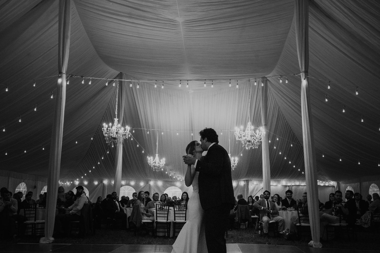 Bride and groom share a tender embrace in a doorway, wearing white gown and navy suit with red boutonniere.