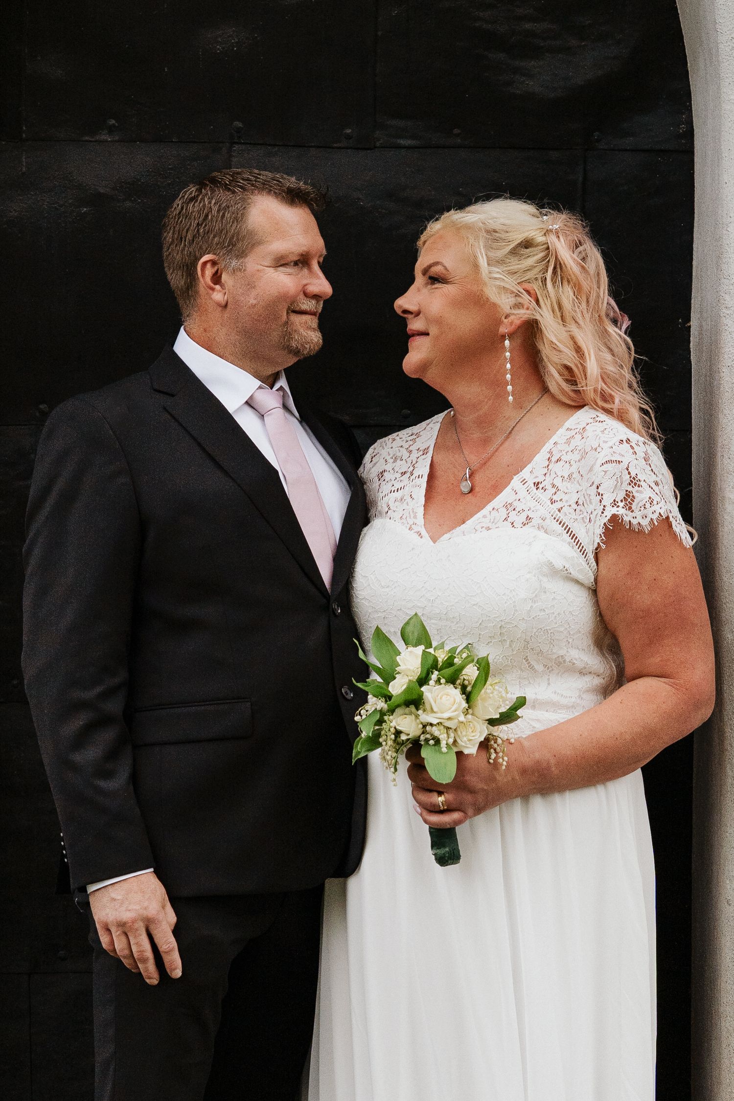 Brudpar ser kärleksfullt på varandra under sin bröllopsfotografering i Kungsgården, Sandviken