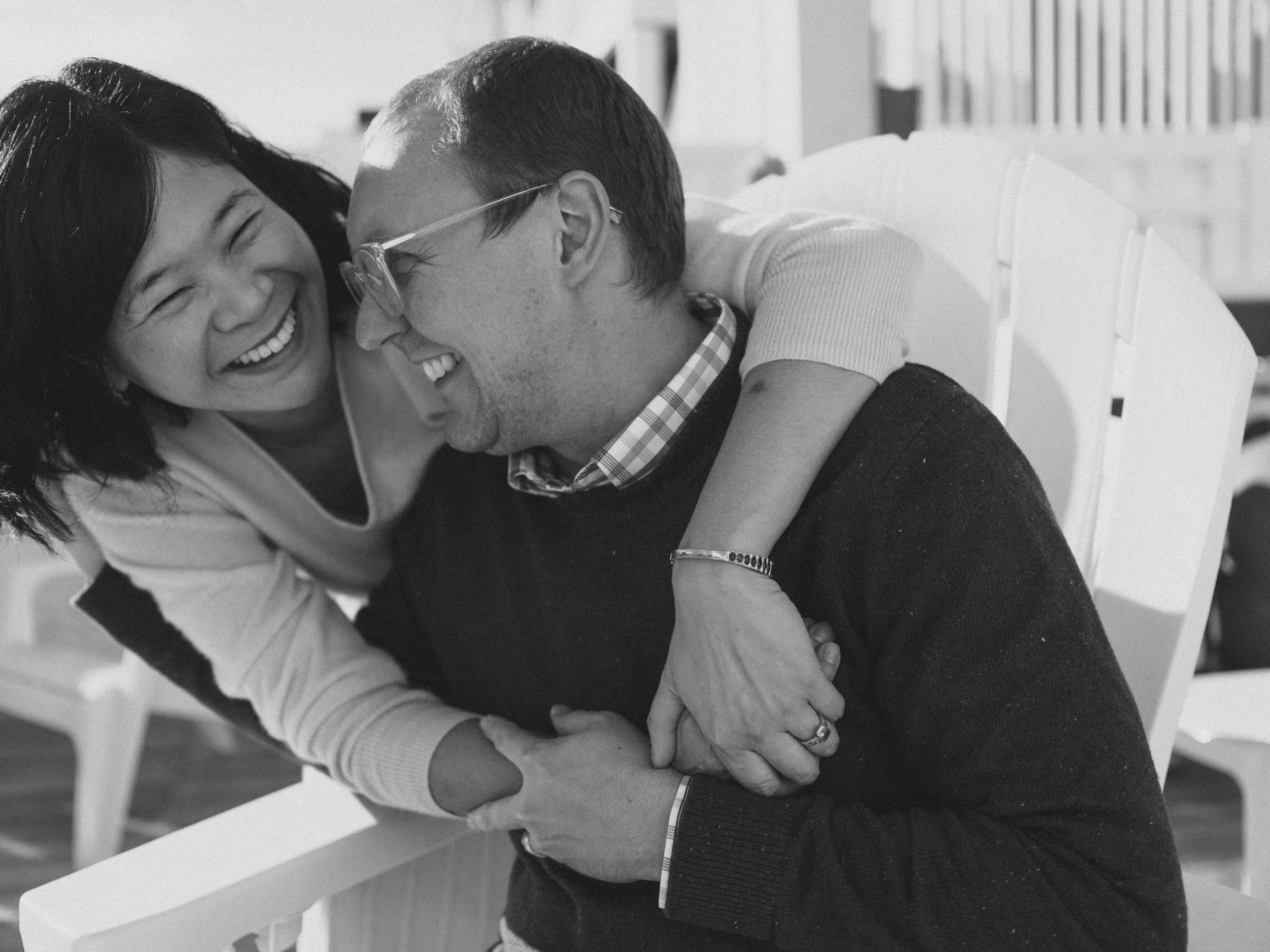 A joyful couple laughing and embracing outdoors in a candid black and white portrait photo.