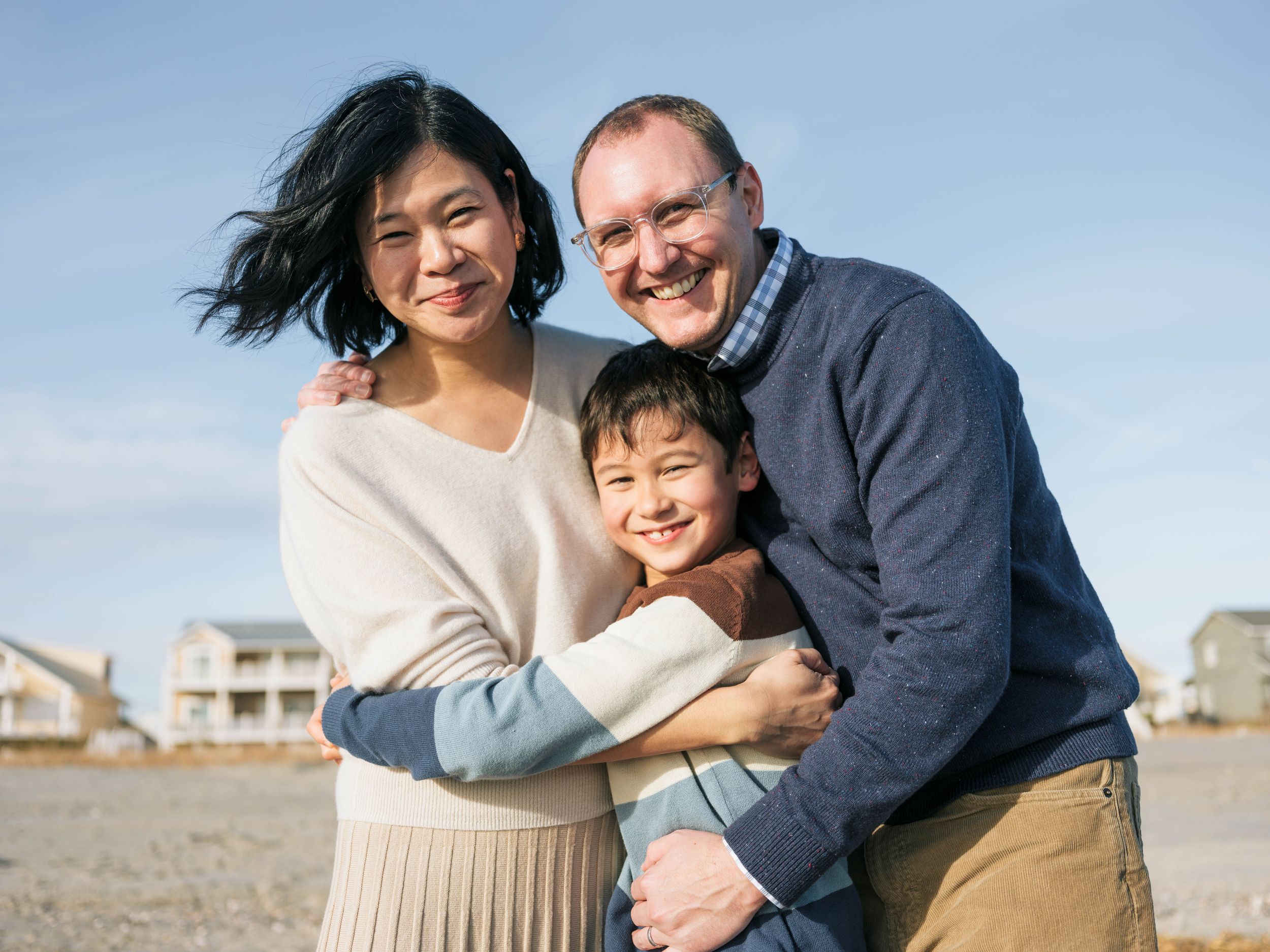 Happy family of three smiling together on a beach on a sunny day with blue skies.