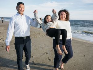 Joyful family playing on the beach as parents swing their young daughter by her arms.