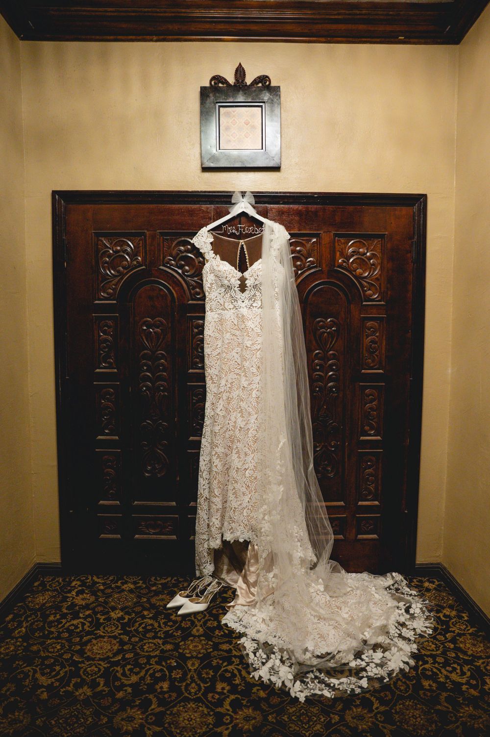 Elegant lace wedding dress with veil displayed on ornate dark wood doors with decorative carved panels.