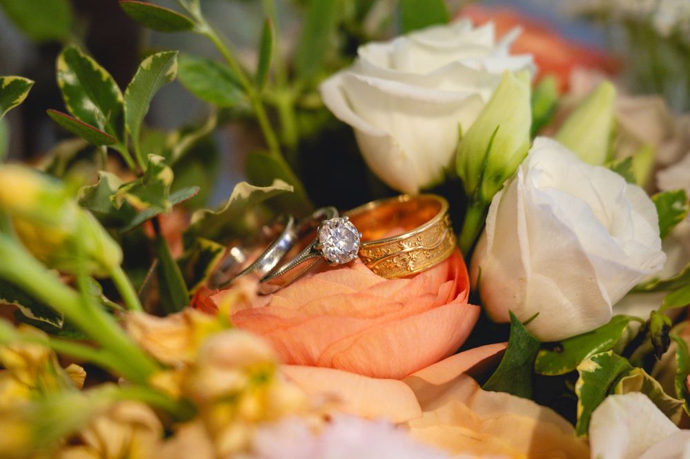 Wedding rings with diamond engagement ring resting on peach rose in bridal bouquet with white roses.