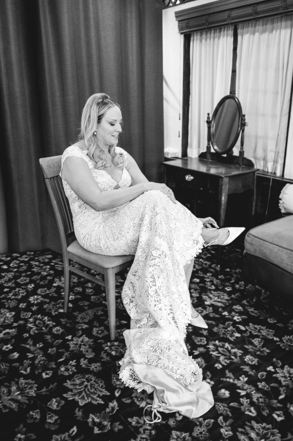 Bride in lace wedding gown sits on chair reading a letter in a black and white photo.