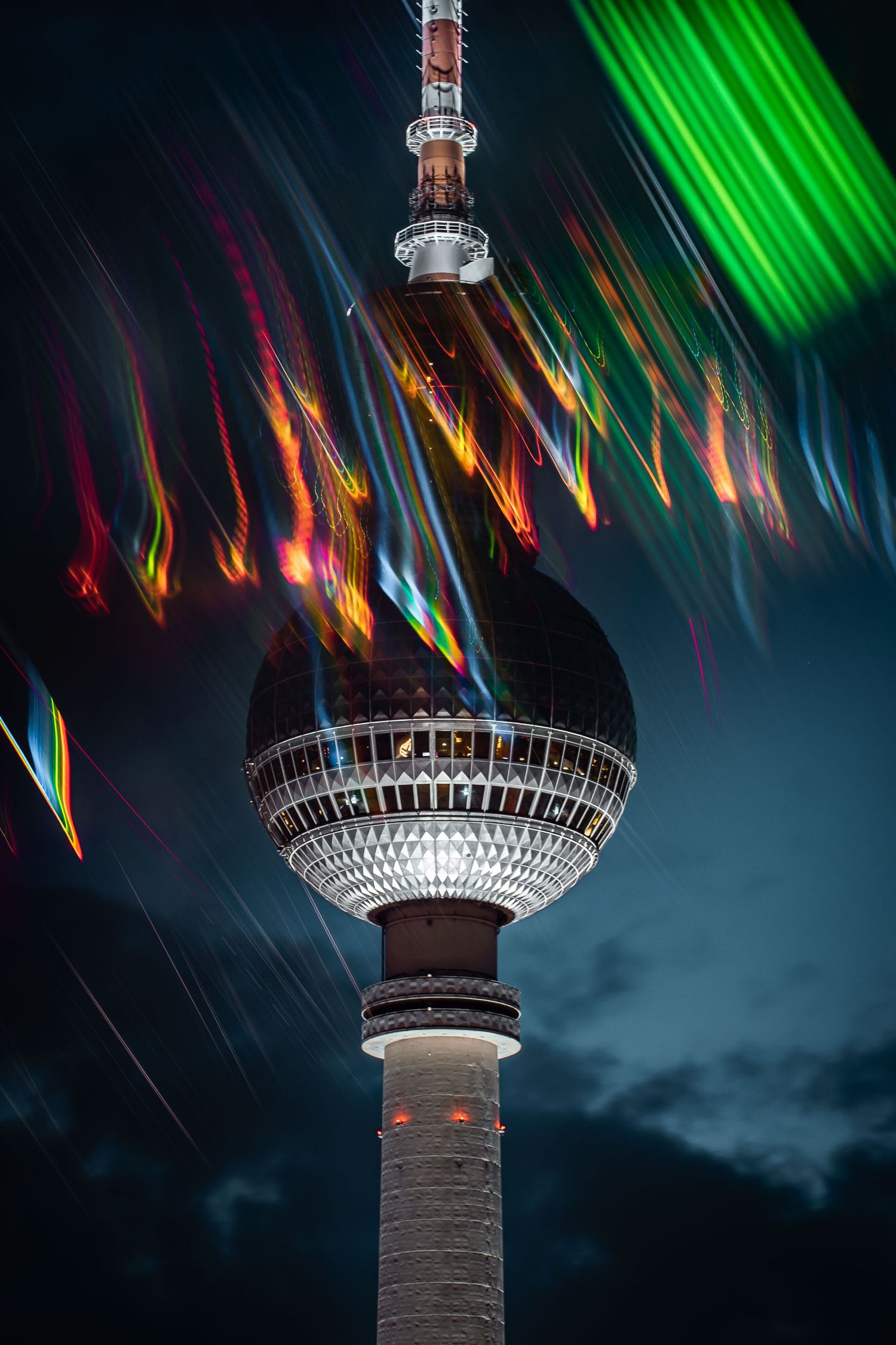 Berlin Victory Column illuminated at night with colorful light trails swirling around the golden statue in a long exposure photo.