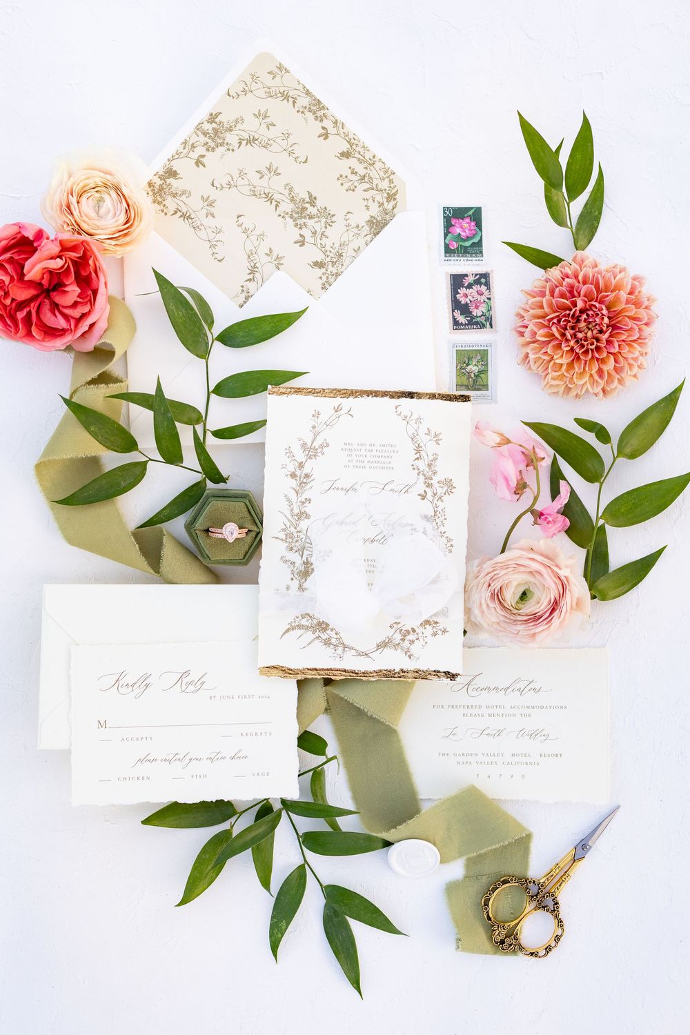 Elegant wedding invitation suite with floral details, greenery, stamps, scissors, and a ring box on a white background.