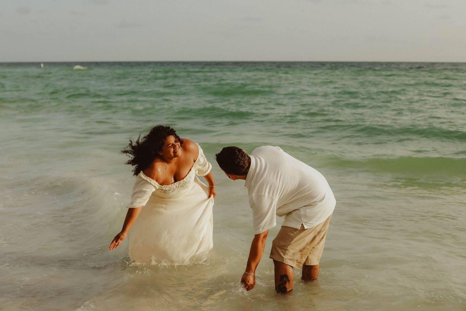 Family in white outfits poses together on a sandy beach with sea oats, sharing a warm moment with babies.